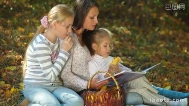 年轻的母亲和两个女儿在秋天的公园野餐读书